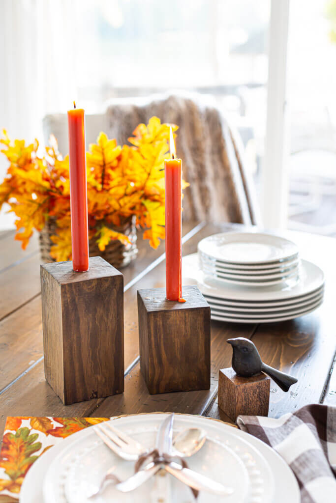 Portavelas de madera de bricolaje completos en una mesa de comedor con velas cónicas de color naranja oscuro.